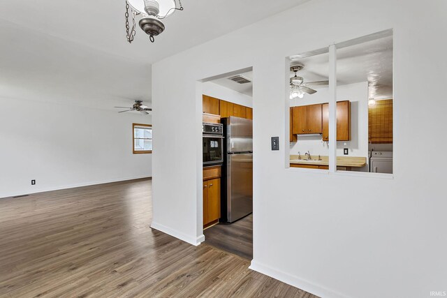 kitchen with brown cabinetry, freestanding refrigerator, visible vents, black oven, and a ceiling fan