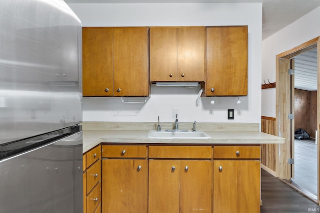 kitchen with brown cabinets, a sink, light countertops, freestanding refrigerator, and dark wood-type flooring