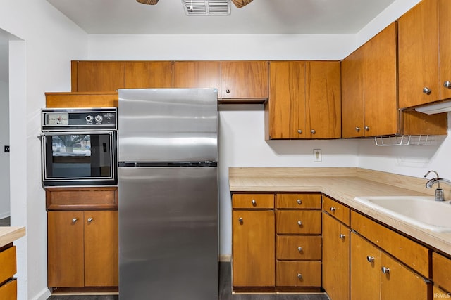 kitchen featuring a sink, light countertops, black oven, freestanding refrigerator, and visible vents