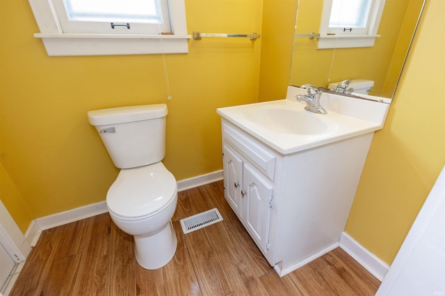 half bathroom with visible vents, vanity, wood finished floors, toilet, and baseboards