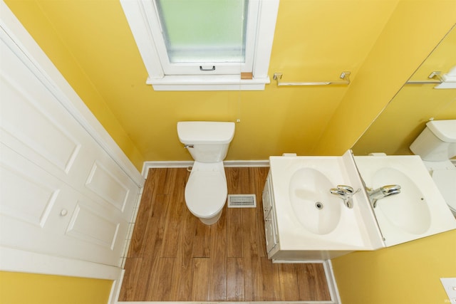 half bathroom with baseboards, wood finished floors, toilet, and vanity
