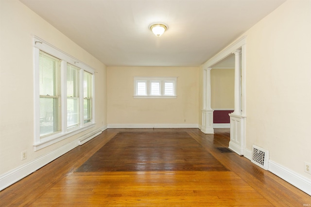 unfurnished room with ornate columns, visible vents, hardwood / wood-style flooring, and a baseboard radiator