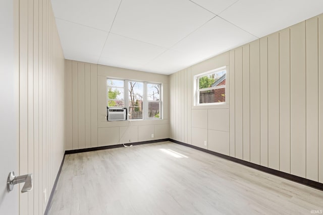 unfurnished room with baseboards, wood walls, wood finished floors, and cooling unit