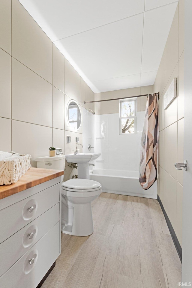 bathroom with wood finished floors, toilet, shower / tub combo, and tile walls