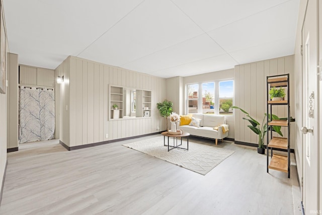 living area featuring baseboards, wood walls, and light wood-type flooring