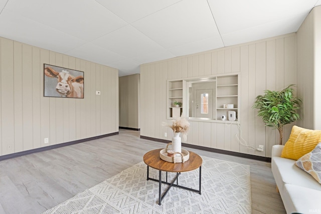 living room with baseboards, built in features, wood finished floors, and wooden walls
