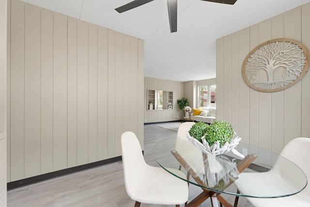 dining area featuring wooden walls, a ceiling fan, baseboards, and light wood finished floors