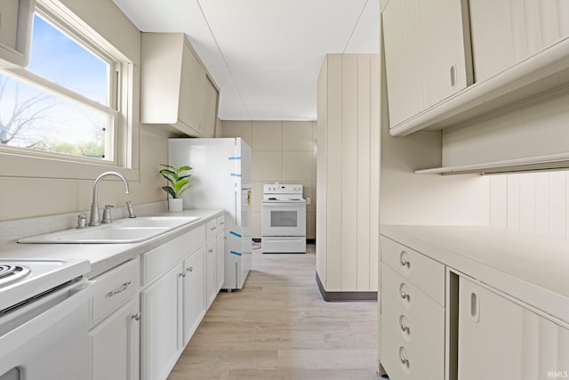kitchen featuring white cabinets, a sink, light wood finished floors, white appliances, and light countertops