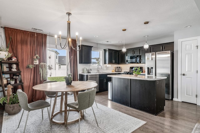 kitchen featuring wood finished floors, a center island, light countertops, a sink, and appliances with stainless steel finishes