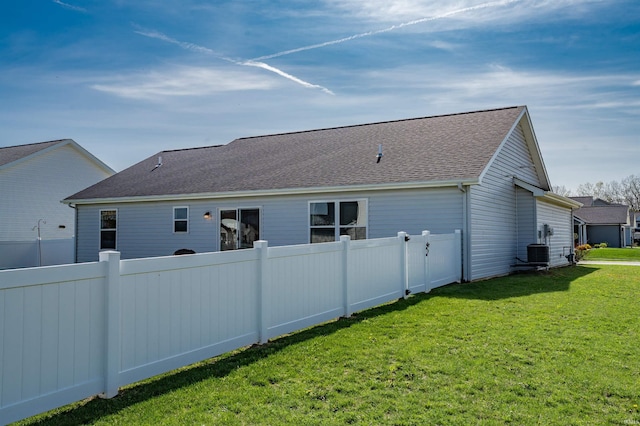 rear view of property featuring a yard, fence, a shingled roof, and cooling unit