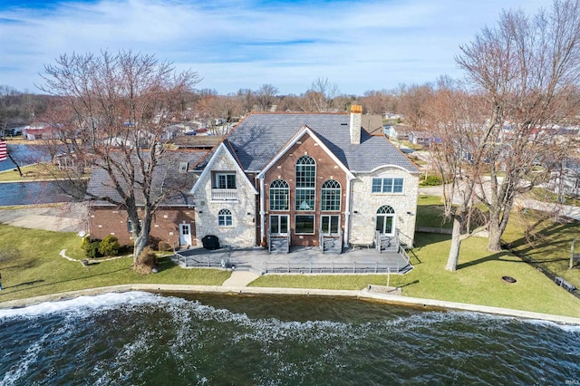 back of house featuring a yard, a patio, a chimney, and stone siding