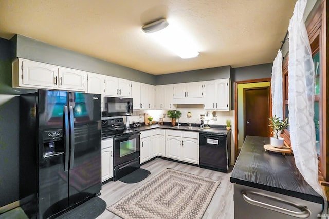 kitchen featuring dark countertops, light wood-type flooring, a sink, white cabinets, and black appliances