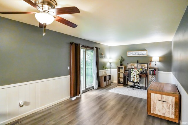 office featuring a ceiling fan, visible vents, wainscoting, and wood finished floors