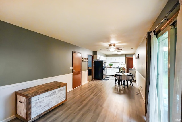 interior space featuring ceiling fan, wood finished floors, and a wainscoted wall
