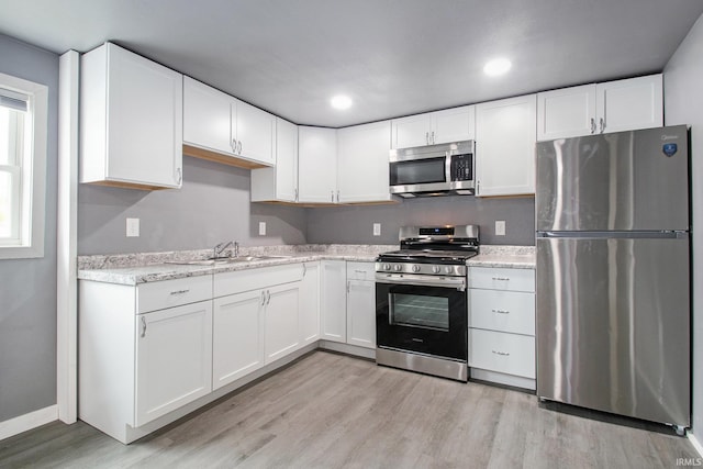 kitchen with a sink, light wood finished floors, white cabinetry, and stainless steel appliances
