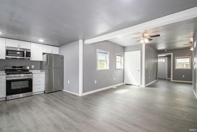 kitchen with baseboards, open floor plan, ceiling fan, light wood finished floors, and stainless steel appliances