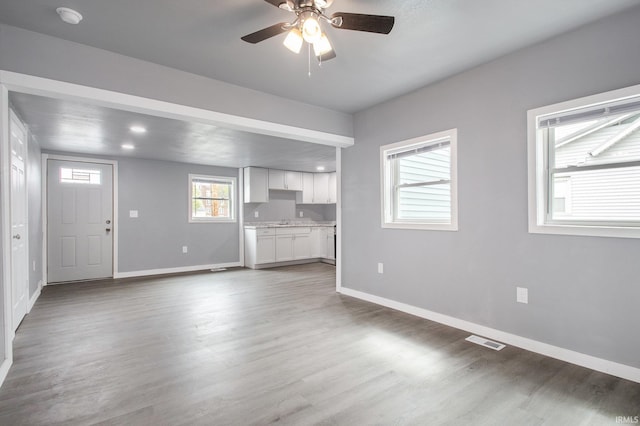 unfurnished living room with baseboards, a ceiling fan, wood finished floors, and visible vents