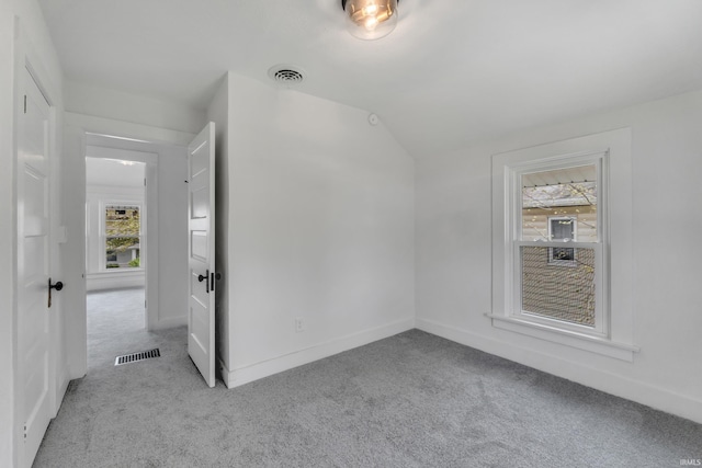 unfurnished bedroom featuring carpet flooring, visible vents, multiple windows, and vaulted ceiling