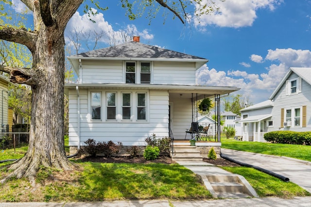 view of front facade featuring a porch, fence, a chimney, and a front yard