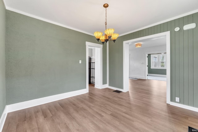 unfurnished dining area featuring an inviting chandelier, baseboards, wood finished floors, visible vents, and ornamental molding