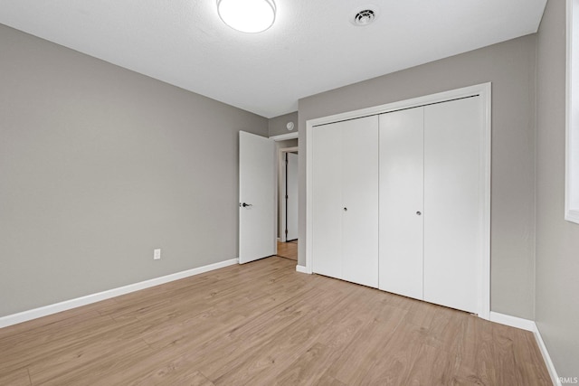 unfurnished bedroom featuring a closet, baseboards, visible vents, and light wood-style floors