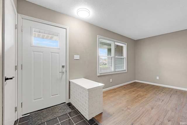 foyer entrance featuring a textured ceiling, baseboards, and wood finished floors