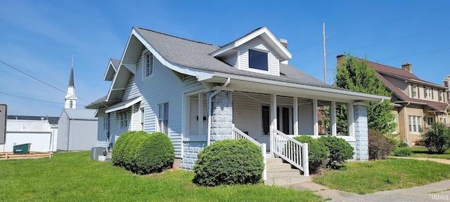 bungalow-style home featuring roof with shingles, covered porch, a front yard, and cooling unit