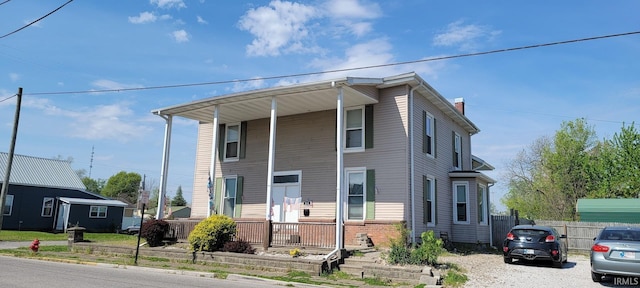 view of front facade featuring covered porch, fence, and a chimney