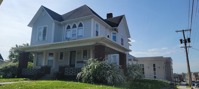 view of front facade featuring a chimney, a porch, and a front yard