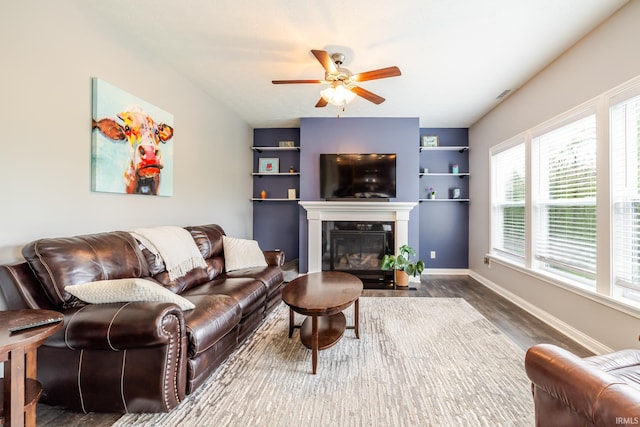 living area featuring ceiling fan, built in features, baseboards, a fireplace with flush hearth, and wood finished floors