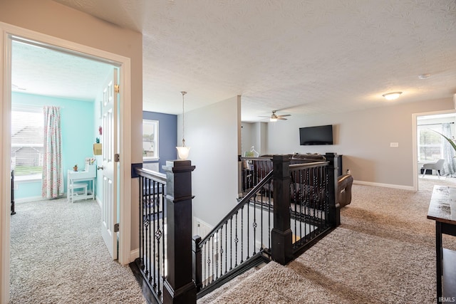 hallway with carpet floors, a textured ceiling, baseboards, and an upstairs landing