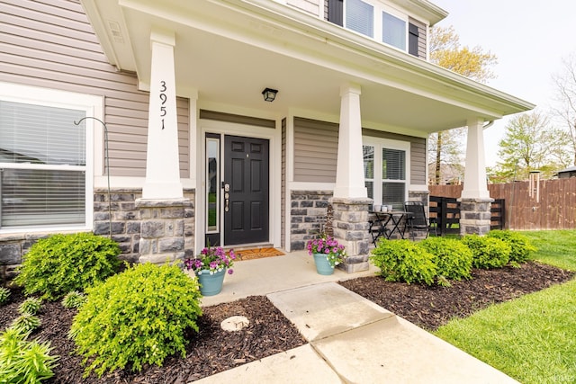 property entrance featuring fence, a porch, and stone siding