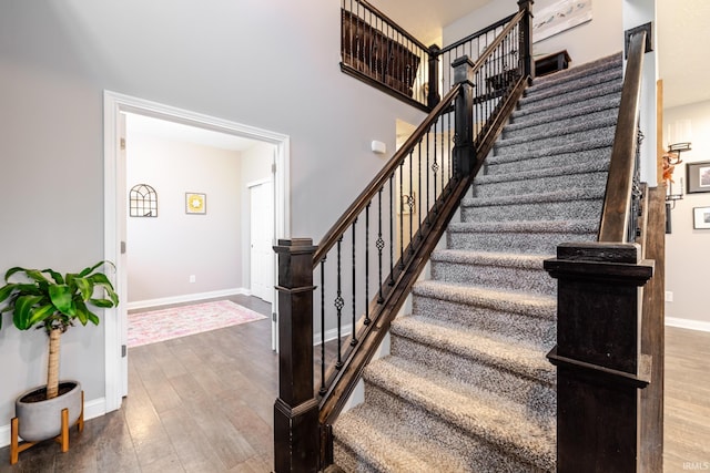 stairs with baseboards, a high ceiling, and wood finished floors