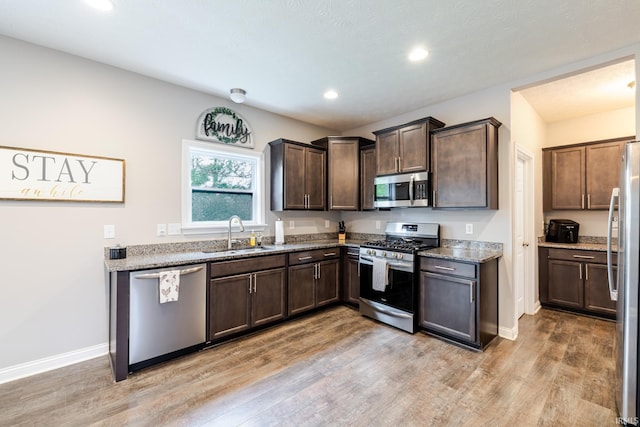 kitchen with dark brown cabinets, light wood-type flooring, a sink, stone counters, and stainless steel appliances