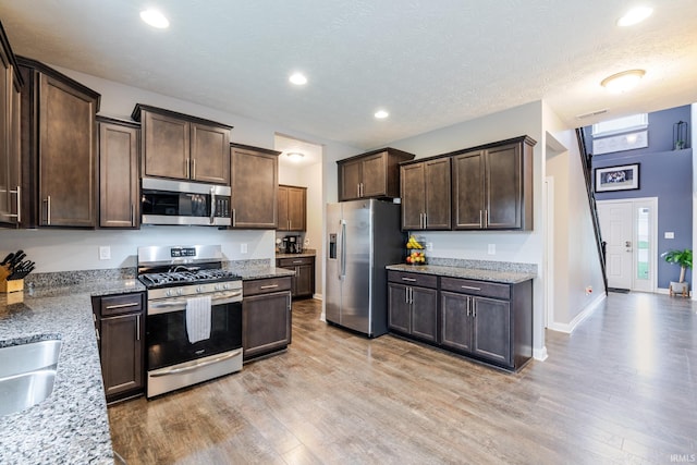 kitchen with appliances with stainless steel finishes, light stone counters, light wood-style flooring, and dark brown cabinets