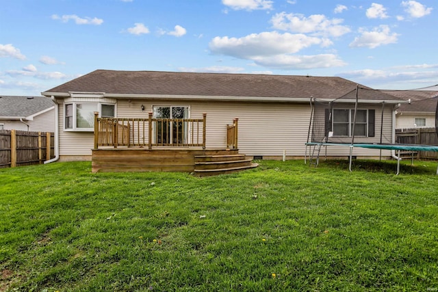 rear view of property featuring a lawn, a fenced backyard, a trampoline, and a wooden deck