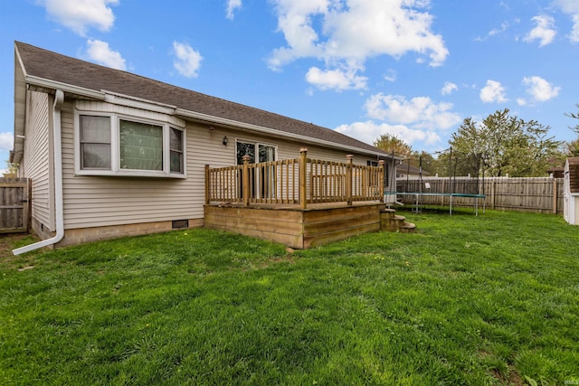 back of house featuring a yard, a wooden deck, a fenced backyard, and a trampoline