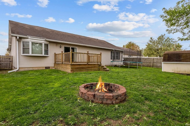 back of property featuring a trampoline, a wooden deck, a shed, an outdoor structure, and a fire pit