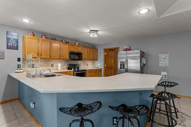 kitchen with appliances with stainless steel finishes, a sink, light countertops, a peninsula, and light tile patterned floors