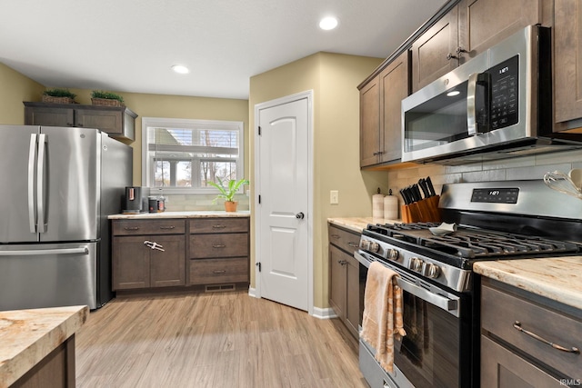 kitchen featuring decorative backsplash, light wood finished floors, dark brown cabinetry, and stainless steel appliances
