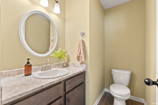 half bathroom featuring toilet, baseboards, wood finished floors, and vanity