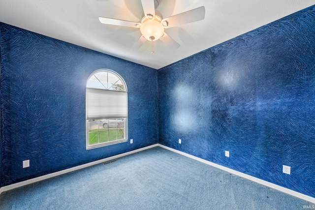 carpeted empty room with baseboards, a ceiling fan, and visible vents