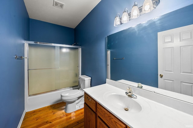 full bathroom featuring shower / bath combination with glass door, vanity, toilet, wood finished floors, and visible vents