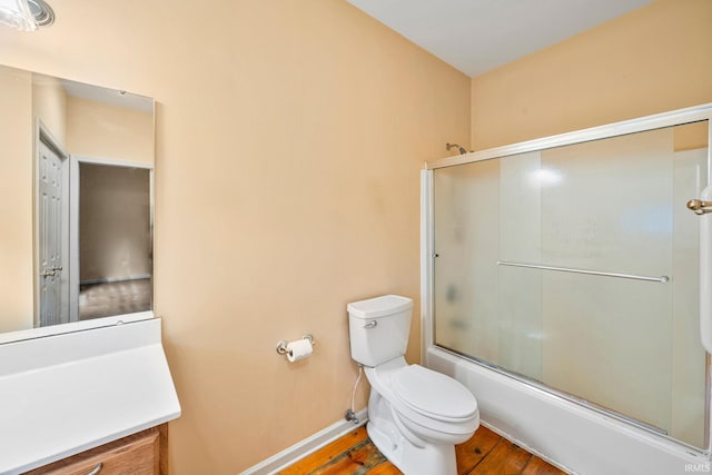 full bathroom featuring wood finished floors, vanity, baseboards, combined bath / shower with glass door, and toilet