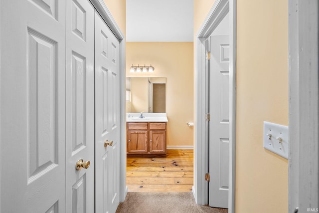hallway with baseboards, a sink, and wood finished floors