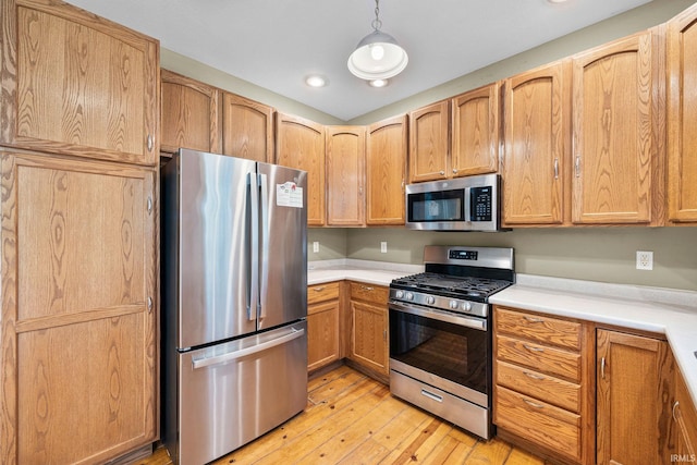 kitchen with light countertops, light wood-style flooring, decorative light fixtures, and stainless steel appliances