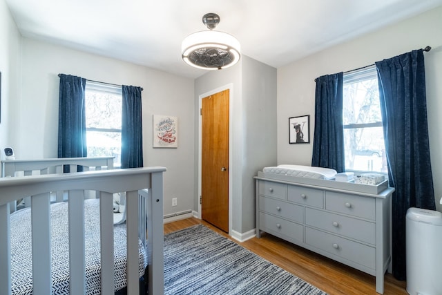 bedroom featuring baseboards, a baseboard heating unit, multiple windows, and wood finished floors