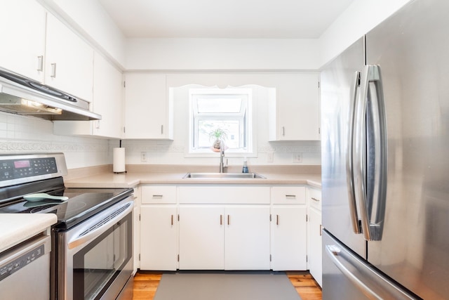 kitchen with light countertops, white cabinetry, under cabinet range hood, a sink, and appliances with stainless steel finishes