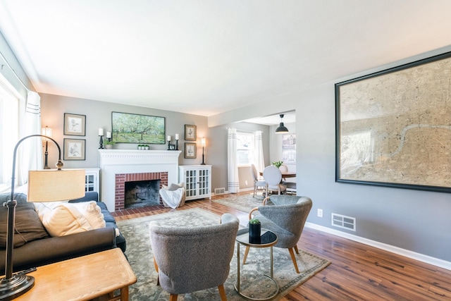 living area featuring baseboards, wood finished floors, visible vents, and a fireplace