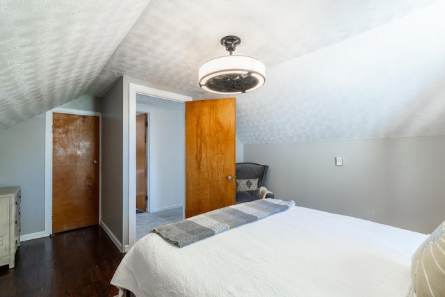 bedroom with baseboards, a textured ceiling, wood finished floors, and lofted ceiling
